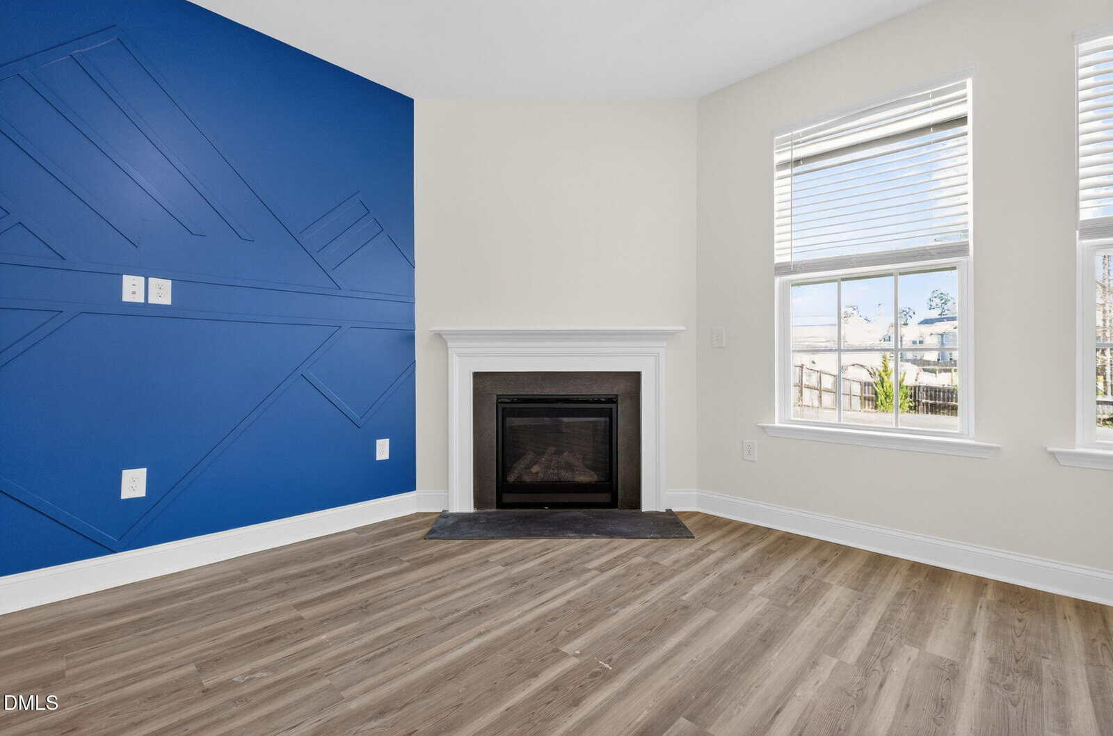 A modern room with wood flooring, a white fireplace, two windows with blinds, and an accent wall painted blue with geometric designs.