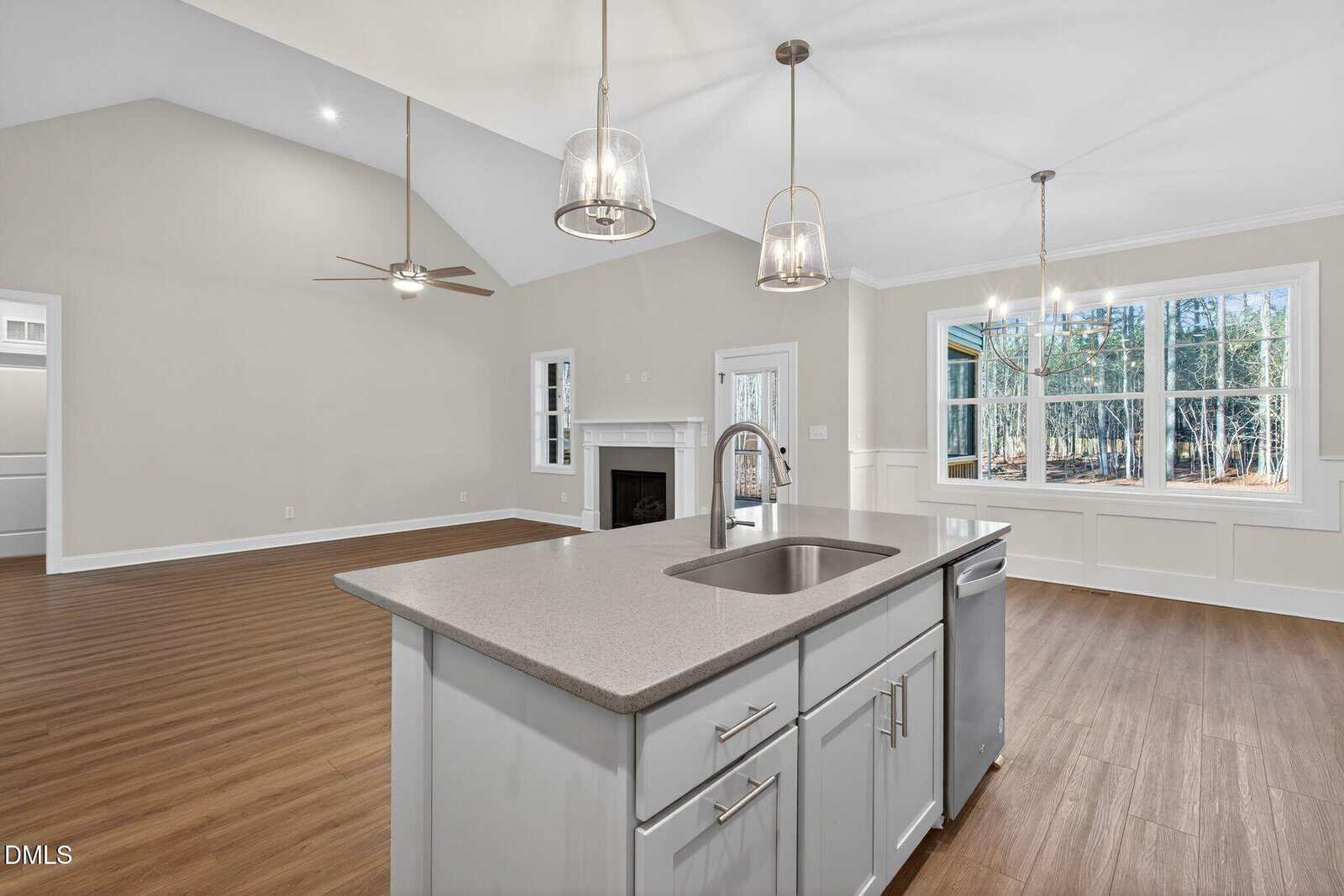 Spacious open-concept kitchen and living area with light gray walls, wood flooring, an island with a sink, a fireplace, ceiling fans, pendant lights, and large windows letting in natural light.