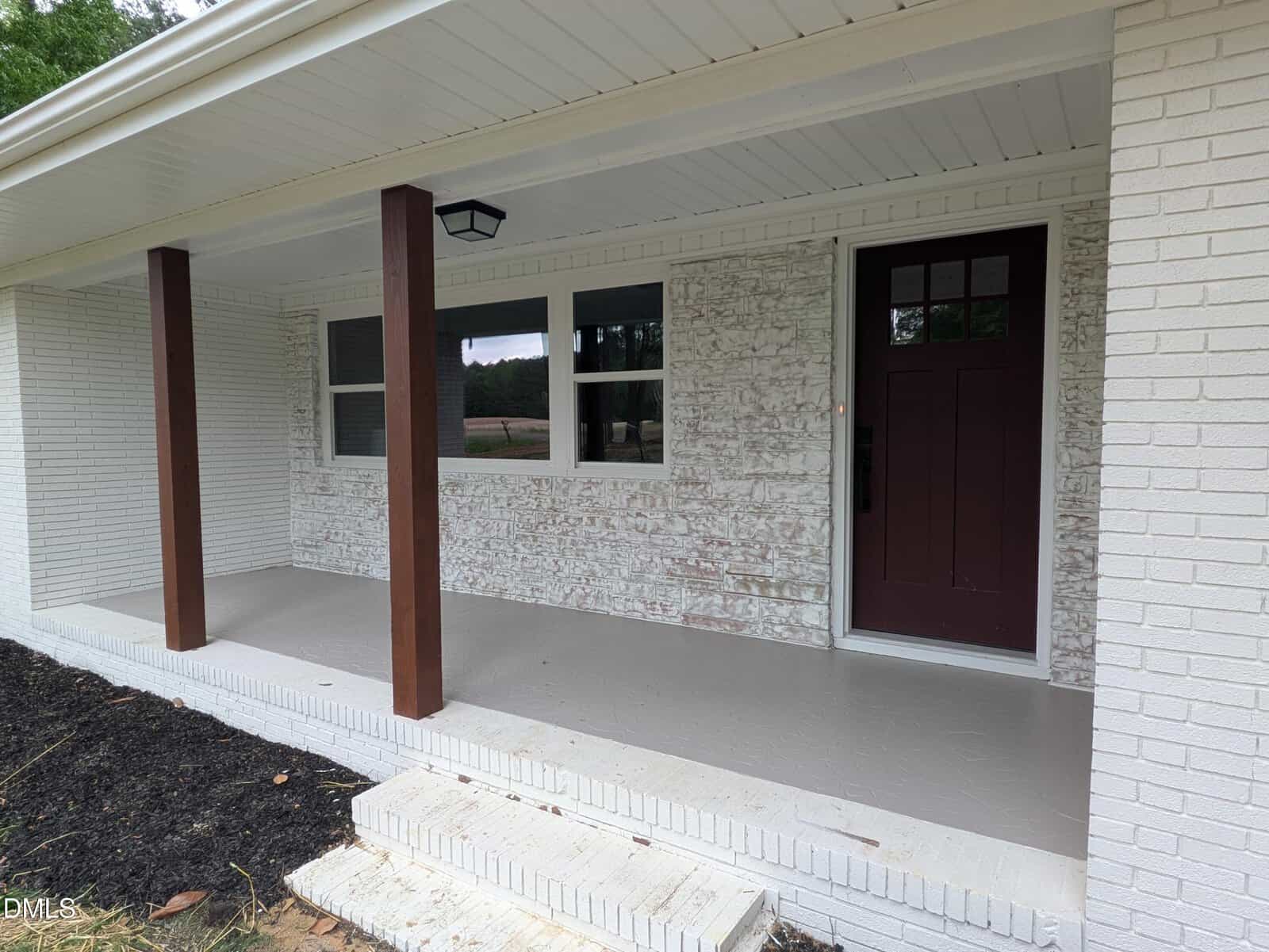 A front porch at 194 Furney Pearce Road in Zebulon features a white painted brick exterior, dark brown columns, a maroon front door with black door hardware, a white ceiling, and a small outdoor light fixture. Black mulch borders the edge of the porch.