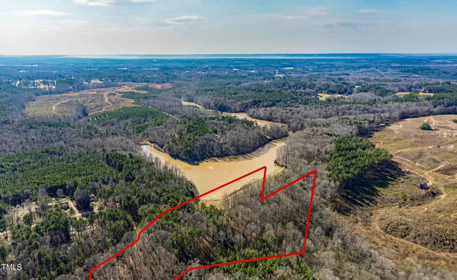 Aerial view of a wooded landscape with a river running through it. A red outline marks the boundaries of a specific parcel of land, which includes both forested and partially cleared areas.