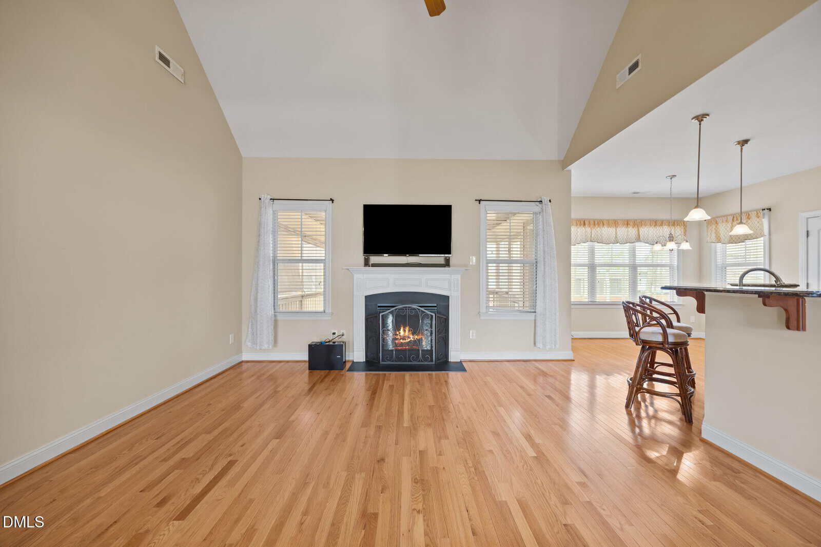 Spacious living room with hardwood floors, a fireplace with a TV above it, large windows with curtains, and a breakfast bar with seating in a bright, open floor plan.