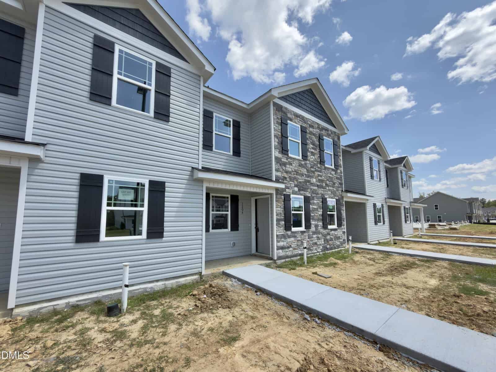 Row of newly constructed two-story townhomes with gray siding and stone accents line 1204 Brookrun Drive in Oxford. Sidewalks and small lawns are visible, with unfinished landscaping and a partly cloudy sky overhead.