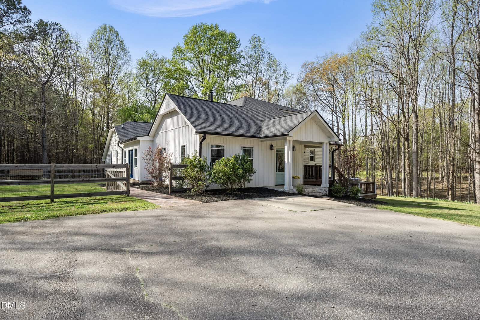 Nestled next to a wooded area in Youngsville, 2566 Mays Crossroad Road features a white single-story house with a dark roof, surrounded by trees and shrubs; a paved driveway leads to the entrance, and a wooden fence lines the yard.