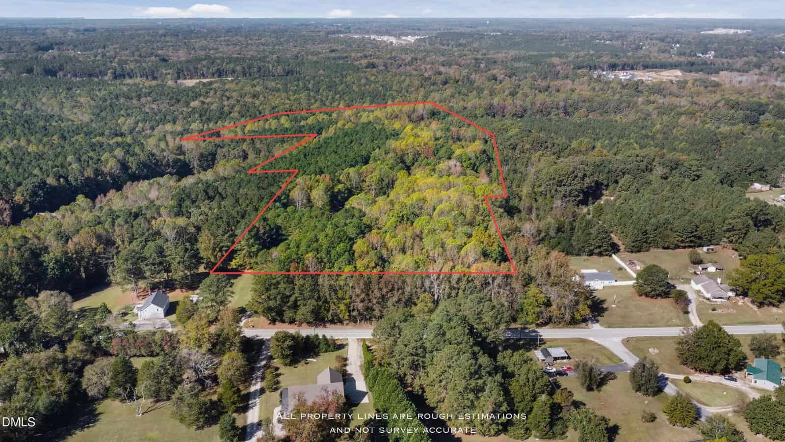 Aerial view of a large, forested plot of land outlined in red, surrounded by more trees and a few houses, with roads and scattered homes visible in the bottom right.