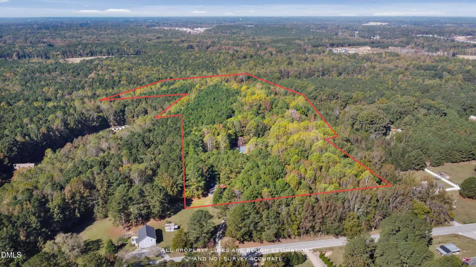 Aerial view of a wooded property outlined in red, surrounded by dense forest and a few scattered homes, with roads visible on the right side of the image.