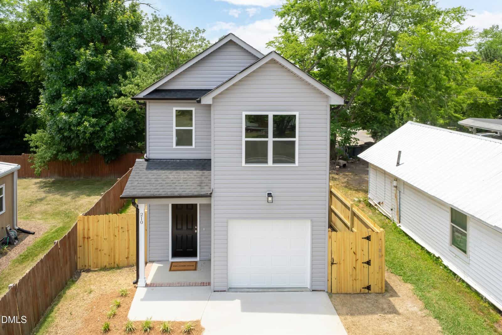 Charming two-story gray house at 210 Orange Street, Oxford features a single-car garage, black roof, and white trim. A wooden fence encloses the backyard, while the front yard boasts a small lawn and young plants.