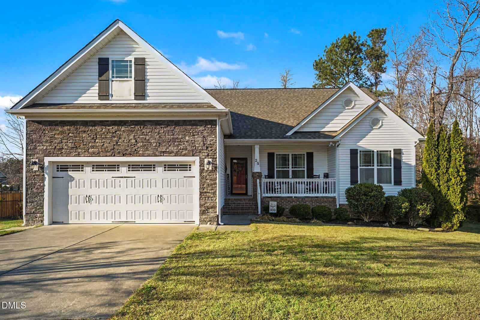 A single-family house with a stone and siding exterior, two-car garage, front porch, and well-kept lawn, set on a sunny day with blue sky and some trees in the background.