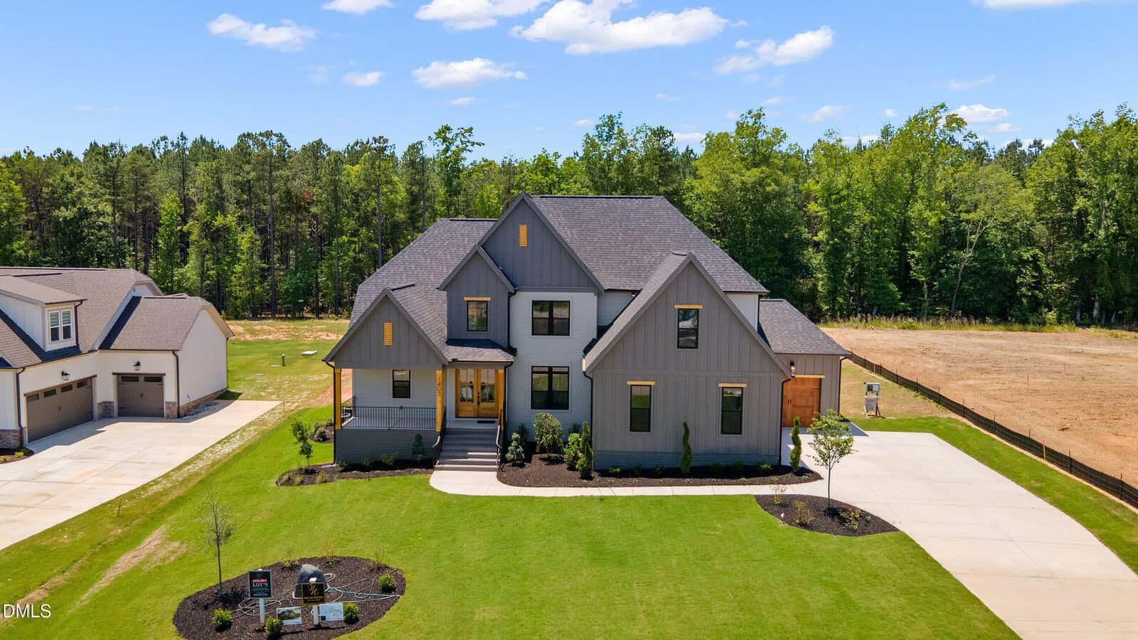 A modern two-story gray house with black trim and a large, neatly maintained front lawn, surrounded by trees and neighboring homes on a sunny day.