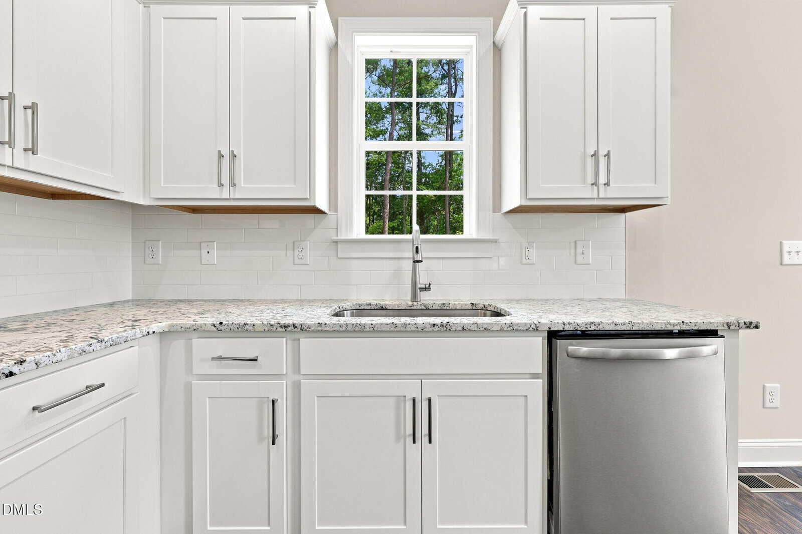 Modern kitchen with white cabinets, a granite countertop, stainless steel dishwasher, sink under a window, and white subway tile backsplash. Natural light comes in through the window above the sink.