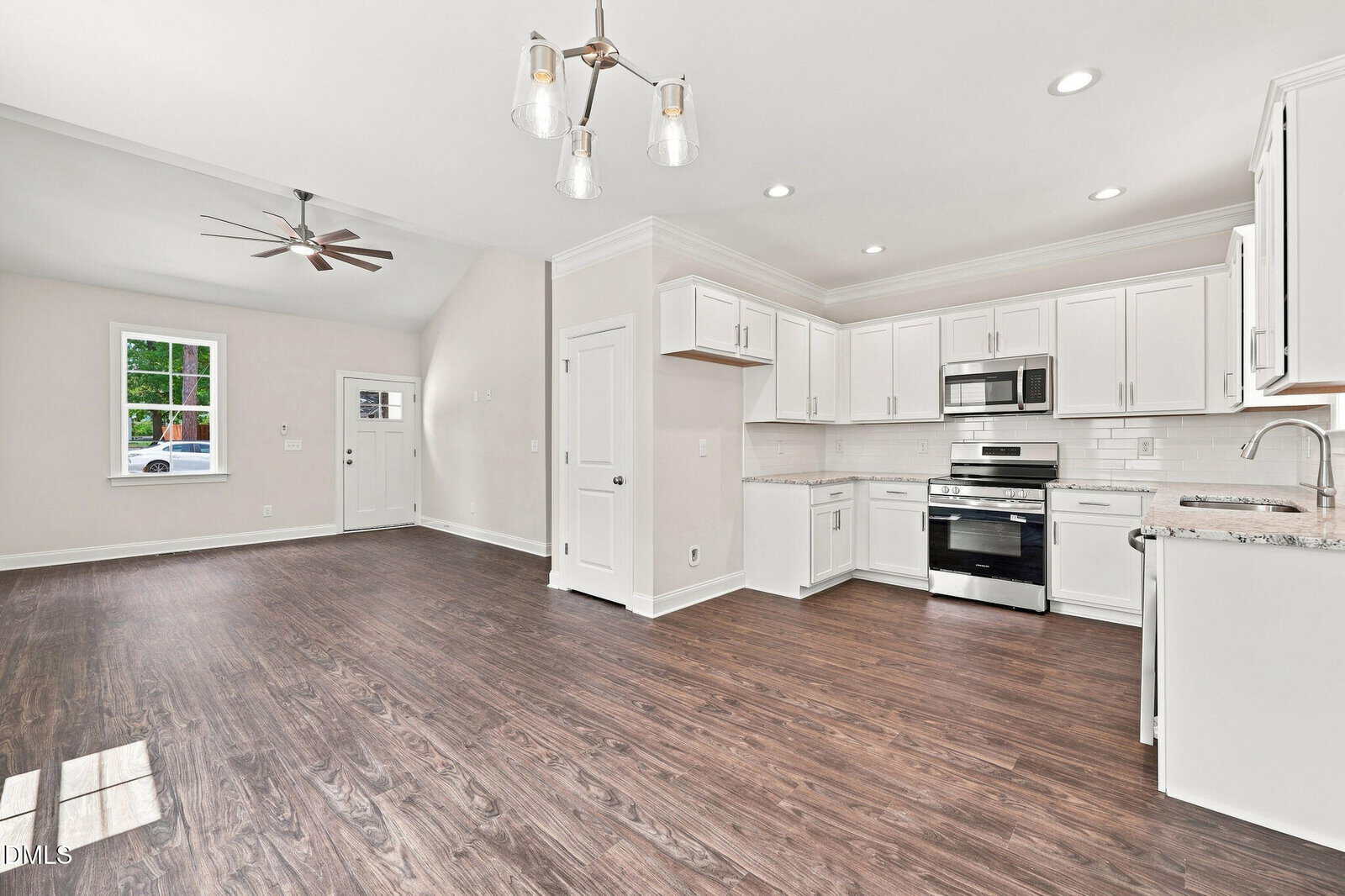 Open-concept kitchen and living area with white cabinets, stainless steel appliances, dark wood floors, recessed lighting, and a modern ceiling fan. A window and door are visible, with neutral-colored walls throughout.