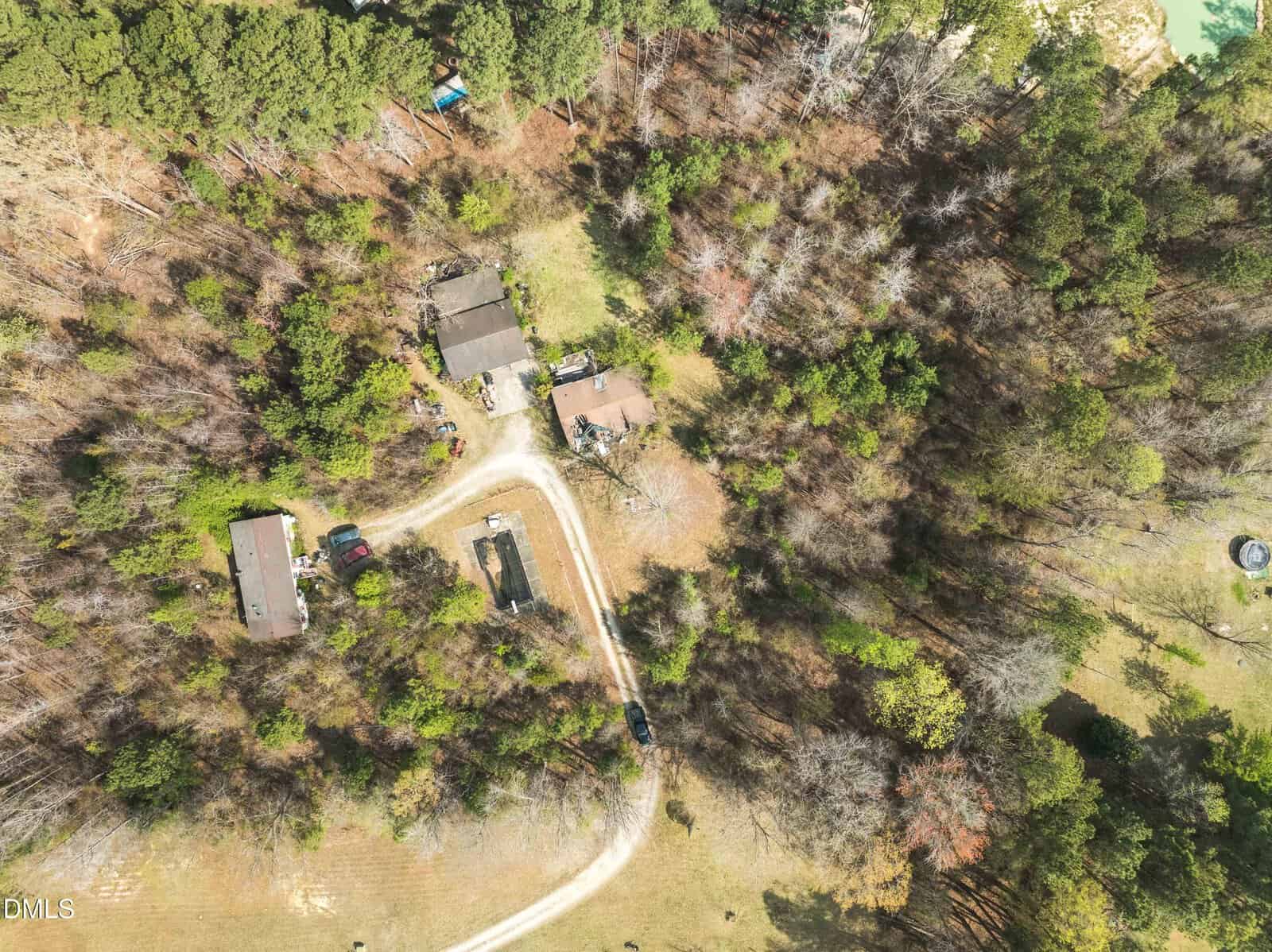 Aerial view of a wooded property with three houses or buildings connected by a curved gravel driveway, surrounded by trees and open grassy areas.