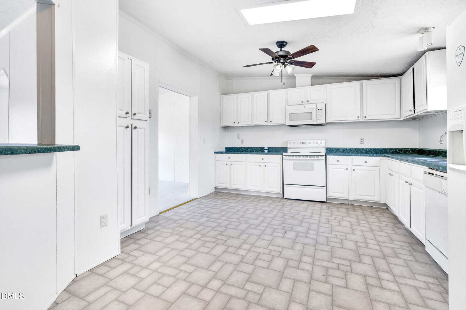 Bright kitchen with white cabinets, white appliances, green countertops, tile floor, and a ceiling fan. A doorway opens to an adjacent room with a white wall and floor.