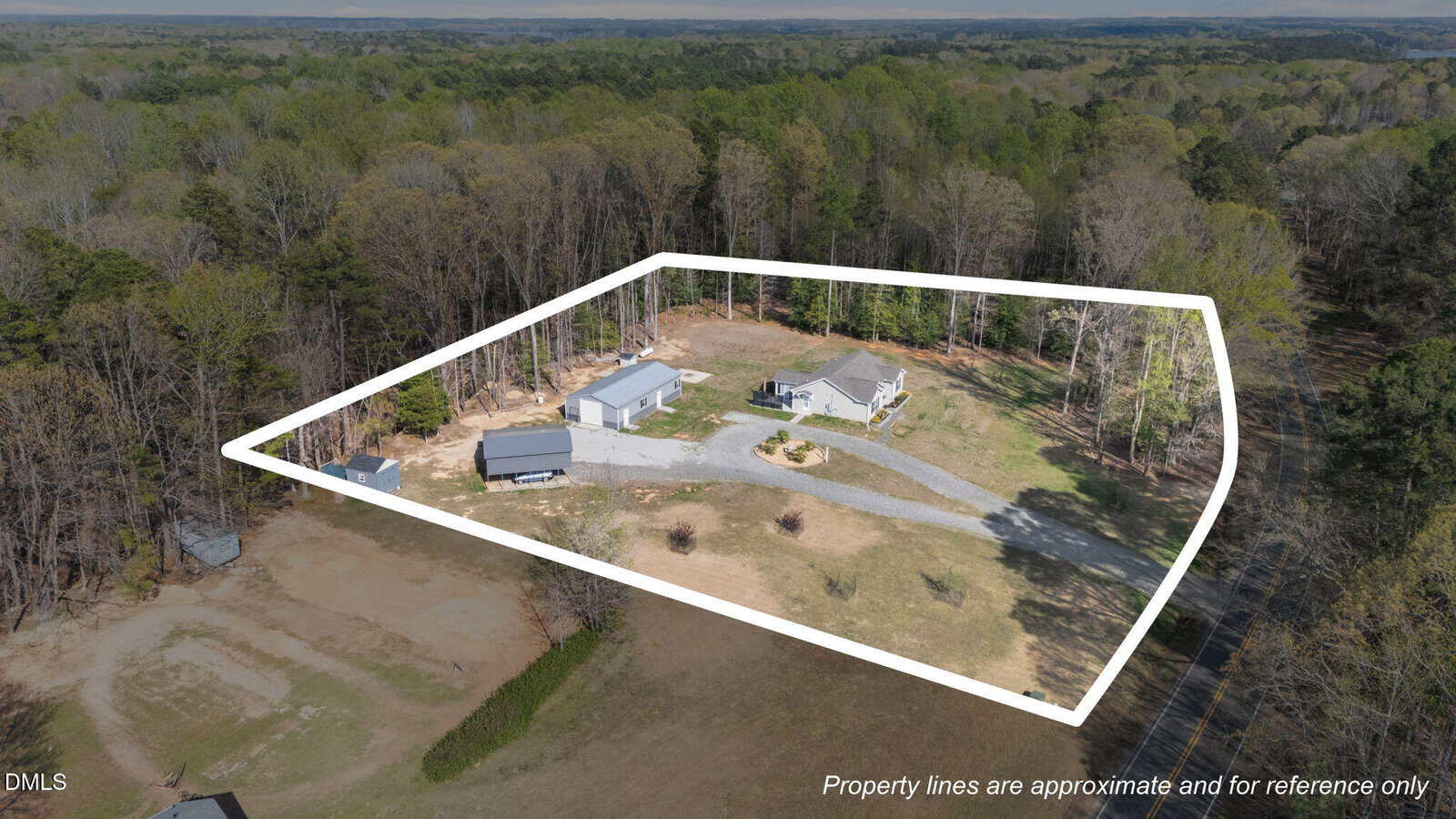 Aerial view of a property outlined in white, featuring a house, a couple of outbuildings, a driveway, grassy areas, and surrounded by trees; note at bottom states property lines are approximate.