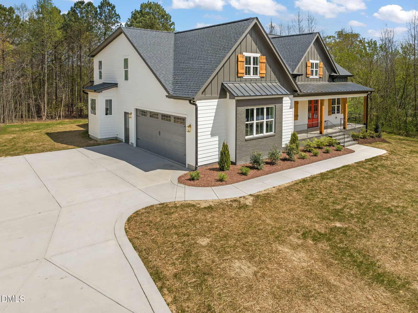 Modern two-story house with a gray roof, white and gray siding, orange window shutters, covered front porch, and a double garage, surrounded by a large yard and bordered by trees in the background.