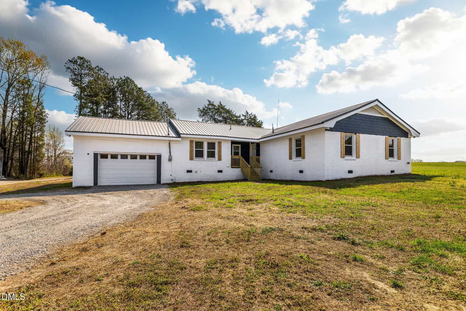 Single-story white house with gray roof, double garage, and small wooden porch; surrounded by grass and trees under a partly cloudy sky in Norlina at 426 Rooker Dairy Road.