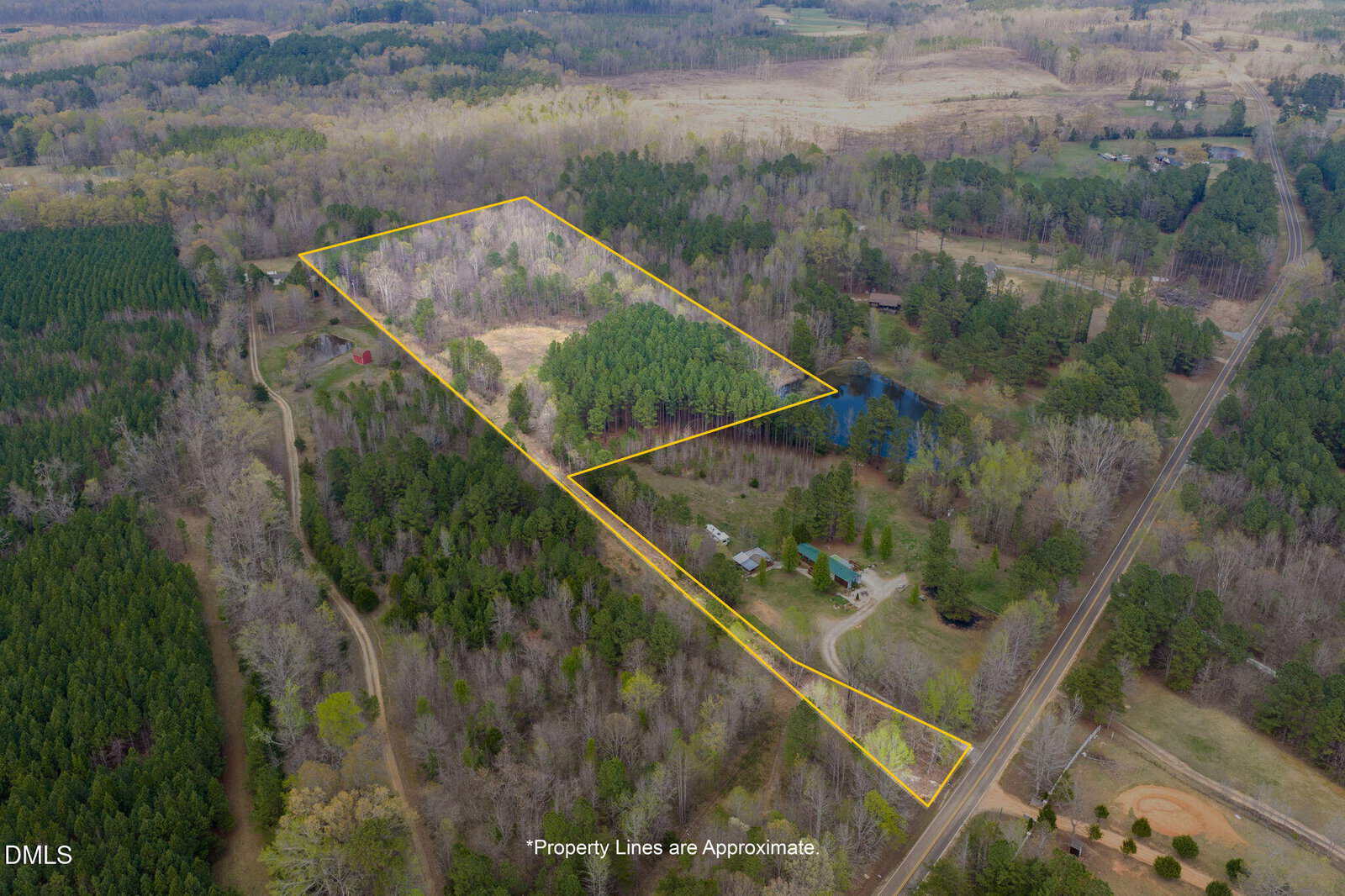 Aerial view of a wooded rural property with approximate boundaries outlined in yellow, including a house, pond, open areas, and trees, surrounded by other forested land and roads.