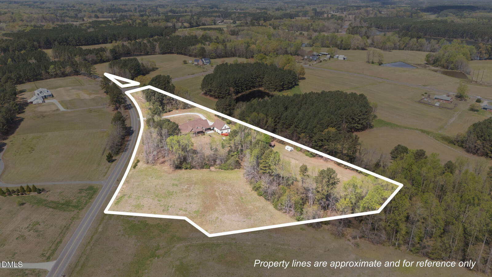 Aerial view of a rural property with a house and trees, outlined in white to show approximate property boundaries. Surrounding areas feature open fields, roads, and clusters of trees. Text notes lines are approximate.