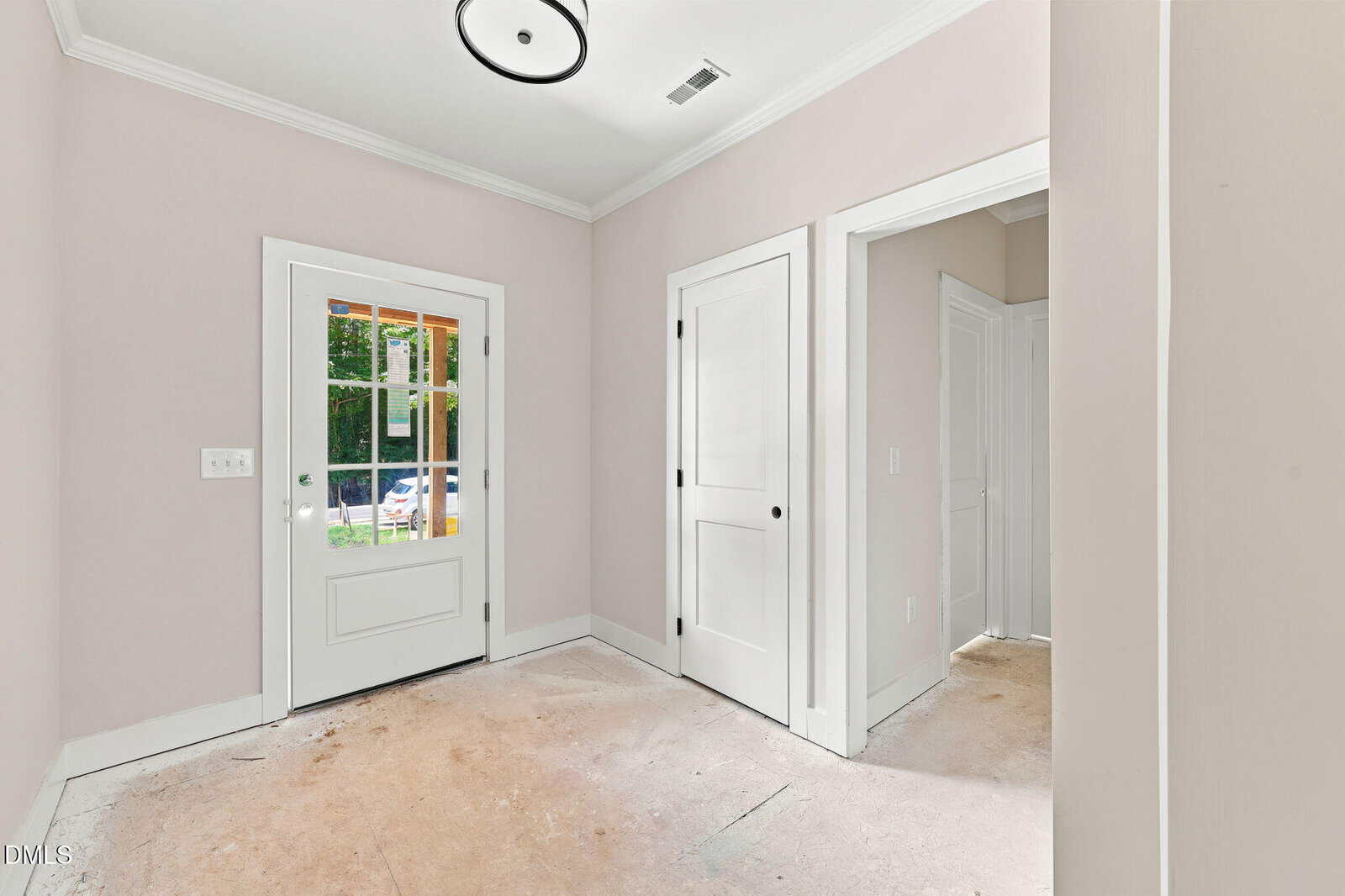 Unfinished entryway with light pink walls, two white doors, a glass-panel door leading outside, ceiling light, and exposed subfloor. Sunlight streams through the glass door, revealing an outdoor space.