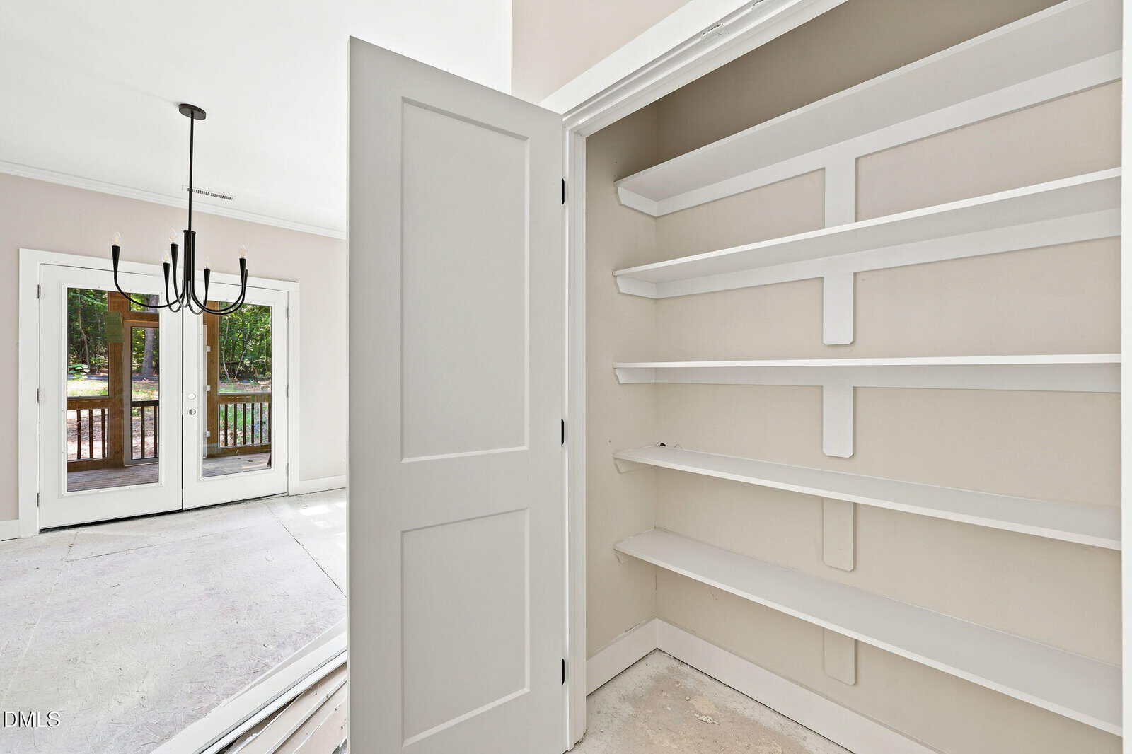 A closet with white built-in shelves is shown next to an open door, leading to a bright room with double glass doors and a black modern chandelier.