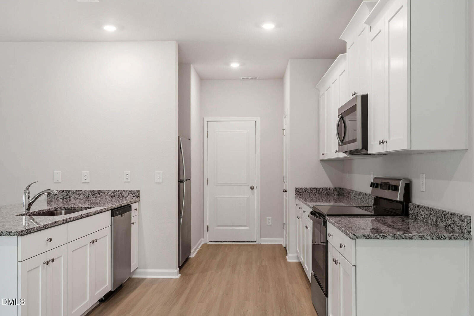 Modern kitchen with white cabinets, granite countertops, stainless steel appliances, and light wood flooring. There is recessed lighting and a door at the end of the room.