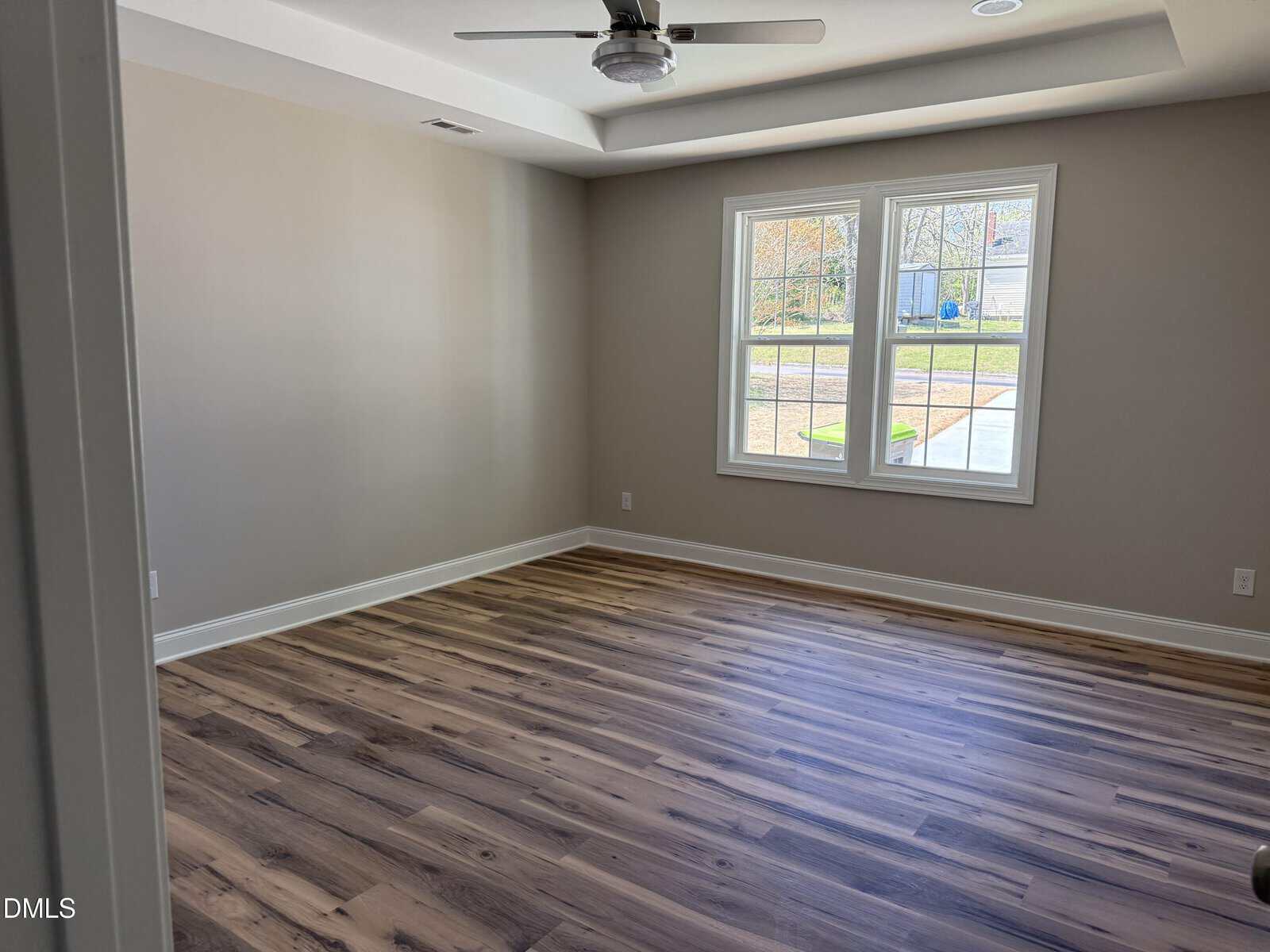 Bright, empty room with light wood flooring, beige walls, a ceiling fan, and a window letting in natural light.