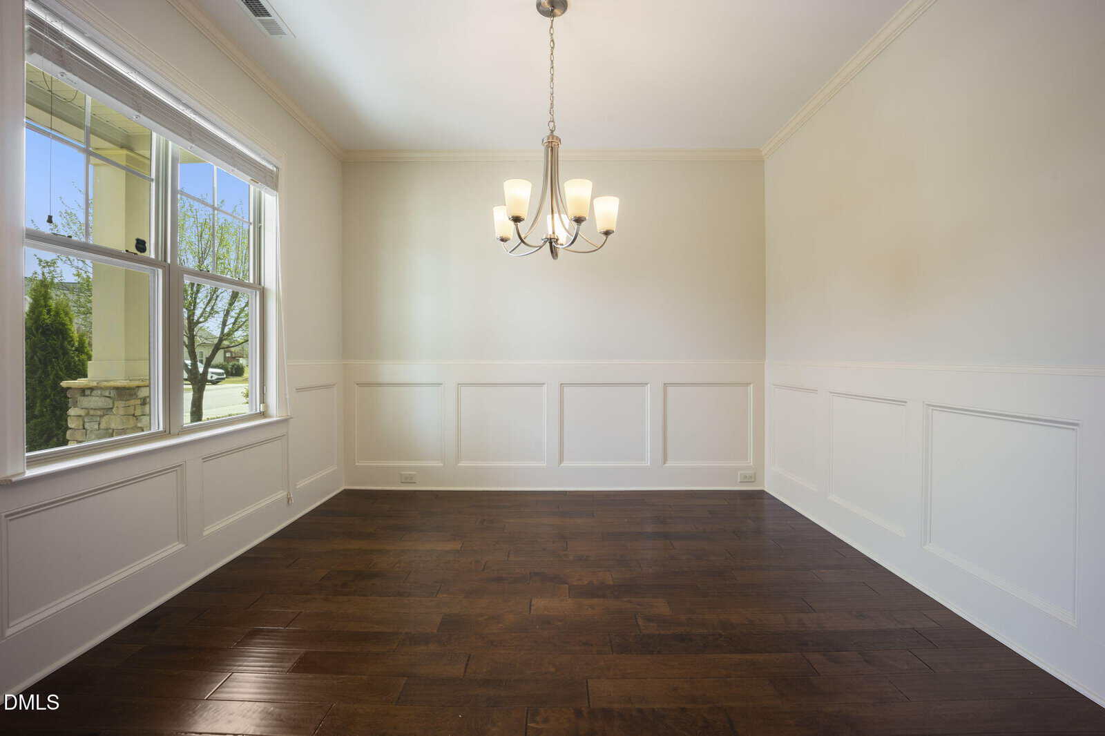 Empty dining room with dark wood floor, white wainscoting, beige walls, a modern chandelier, and a large window letting in natural light.