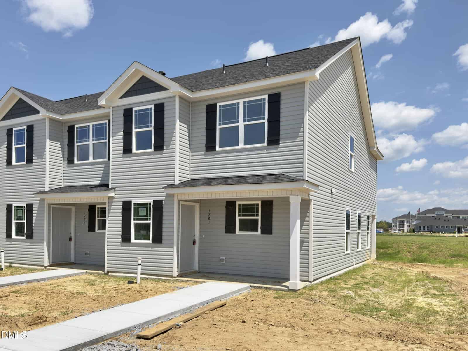 A newly built two-story townhouse at 1201 Brookrun Drive, Oxford, featuring gray siding, black shutters, and white trim. The house is situated on a corner lot with unfinished landscaping and a clear blue sky in the background.