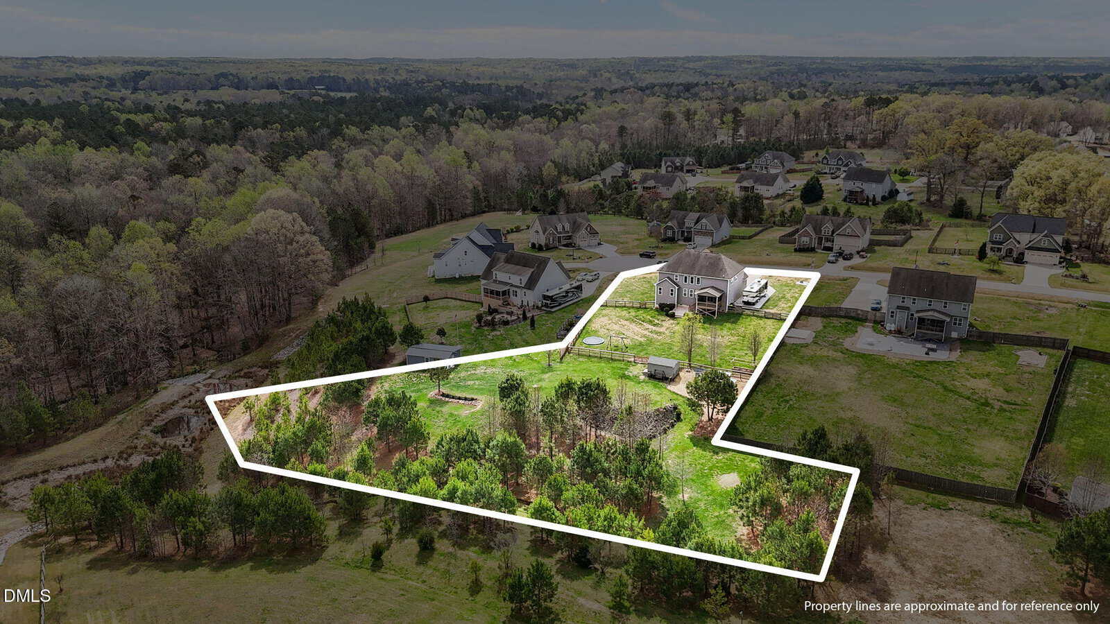 Aerial view of a suburban neighborhood with a white outline highlighting a large, irregularly shaped property that includes grassy and wooded areas behind a house.