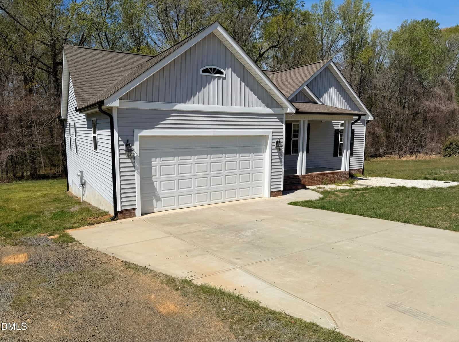 Nestled at 987 Red Stone Court in Rougemont, this light gray single-story house features white trim, a two-car garage, and a spacious concrete driveway. The gable roof and small front porch complete the inviting setting amid grass and trees.