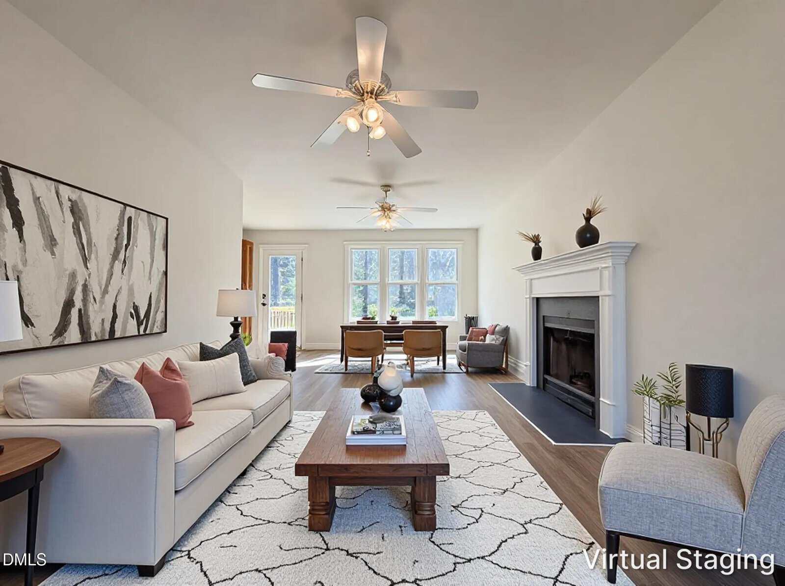 A bright, modern living room with a white sofa, armchair, abstract art, ceiling fans, a fireplace, and large windows letting in natural light. "Virtual Staging" is labeled in the bottom right corner.