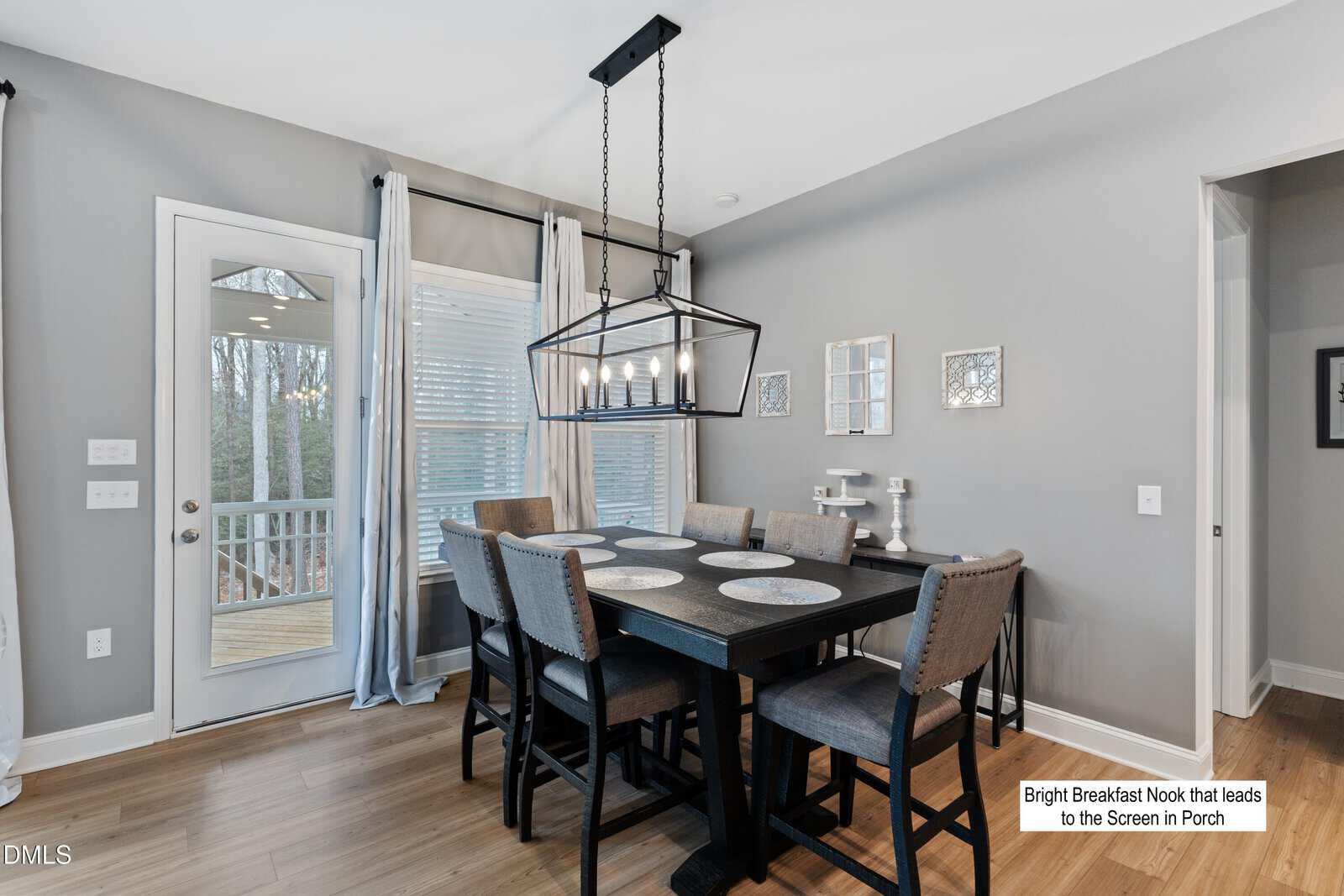 Modern breakfast nook with a black rectangular table and six cushioned chairs, large windows, gray walls, and a door leading to a screened-in porch. A black chandelier hangs above the table.