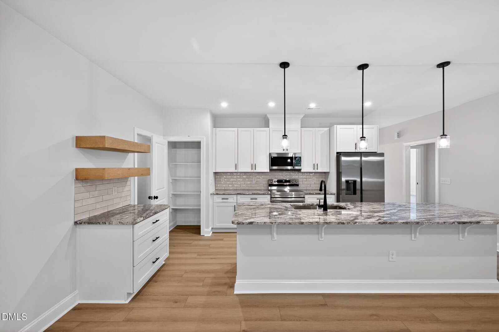 Modern kitchen at 244 Sequoia Drive in Louisburg with white cabinets, stainless steel appliances, marble island with sink, pendant lights, open wooden shelves, and light wood flooring. Decor is minimal and bright with a clean, contemporary design.