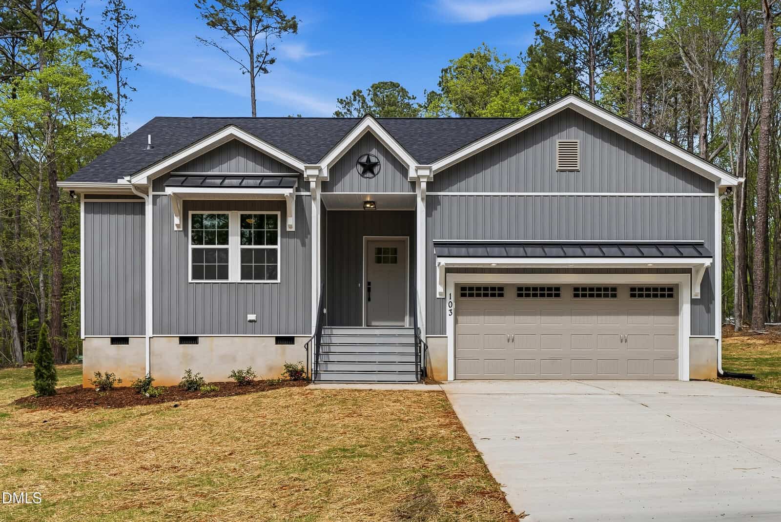 Charming gray single-story house at 103 Fort Drive in Louisburg with white trim, a front porch, attached two-car garage, freshly laid driveway, and straw-covered yard surrounded by trees.