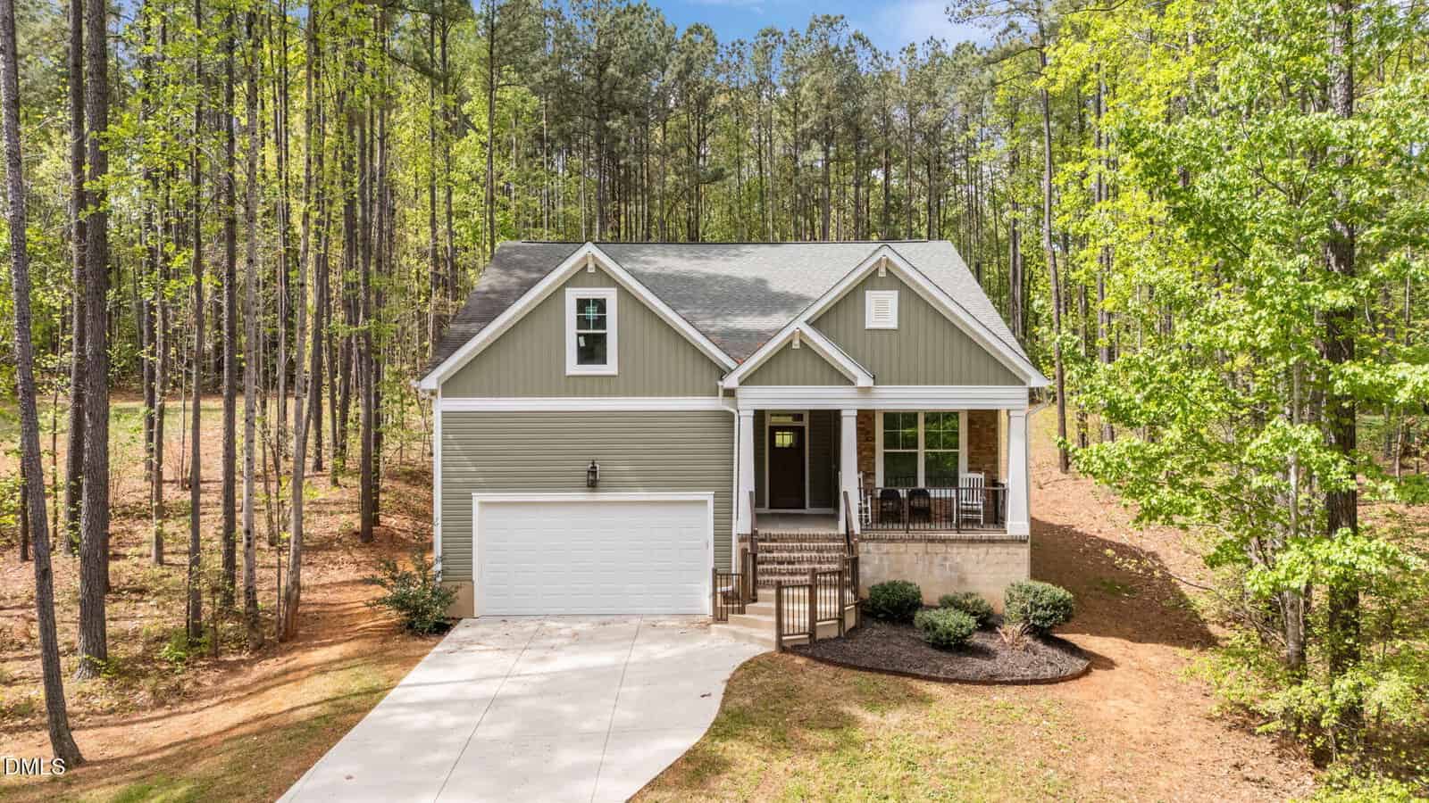 Located at 4537 Gresham Drive in Oxford, this single-story house features a gray exterior with white trim and a welcoming front porch. A two-car garage and concrete driveway add convenience, while tall trees surround the home on its wooded lot, creating a serene setting.