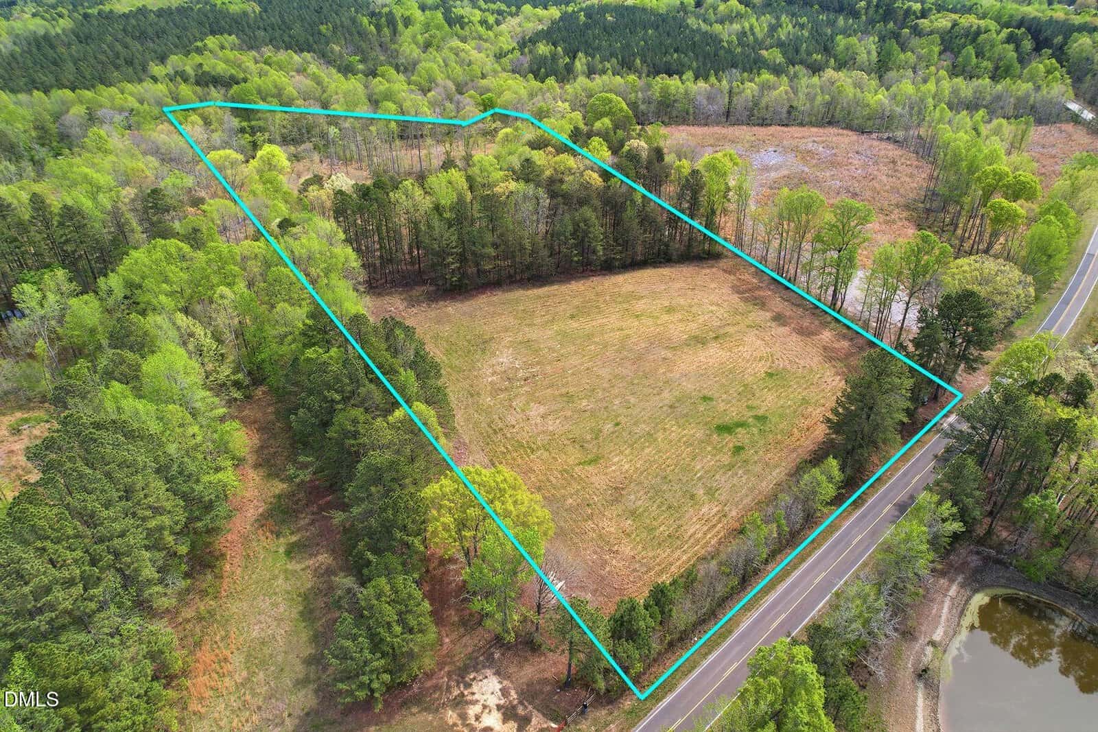 Aerial view of a rectangular, partially wooded plot of land at 6134 Bob Daniel Road, Oxford, bordered by a blue outline, showing grassy and forested areas, a road along one side, and surrounding trees.