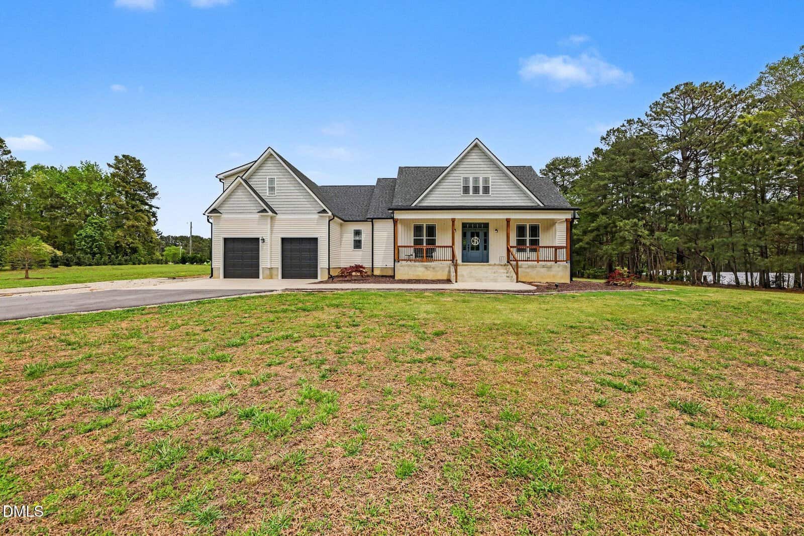 A white two-story house with a front porch, two black garage doors, and a large grassy yard is nestled at 127 Morgan Drive in Zebulon, surrounded by trees under a clear blue sky.