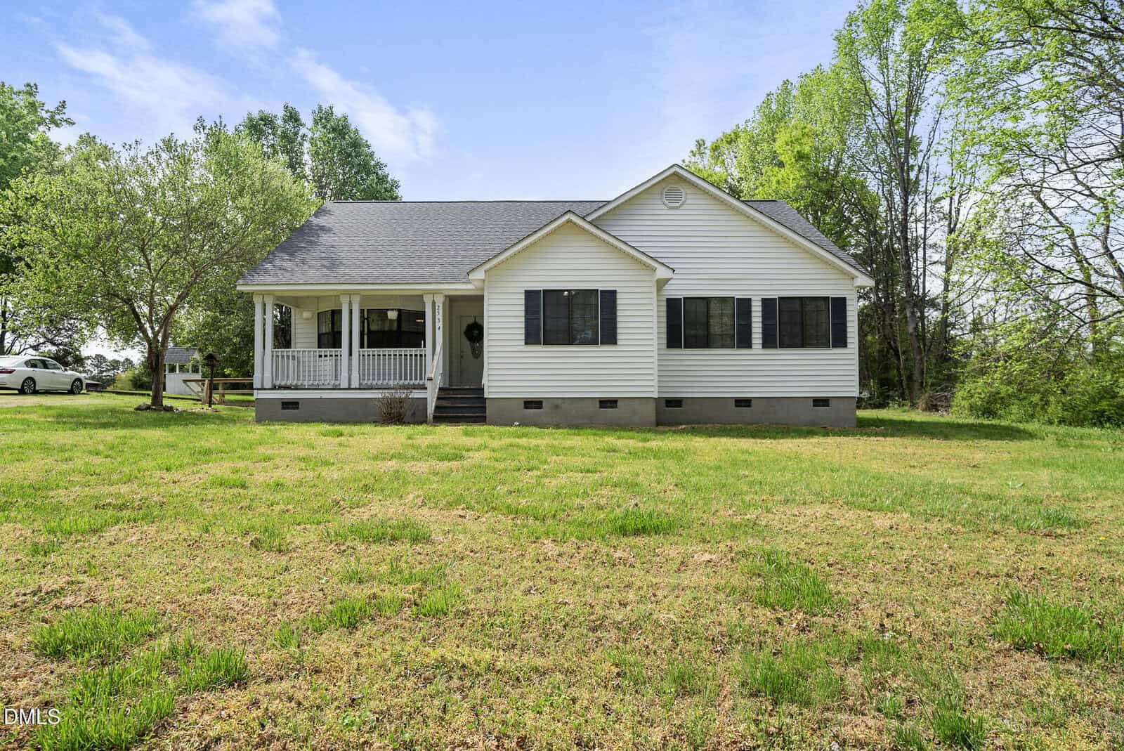 A white single-story house with a front porch, black shutters, and a gray roof sits on a grassy yard surrounded by trees under a partly cloudy sky at 2534 Enon Road, Oxford.