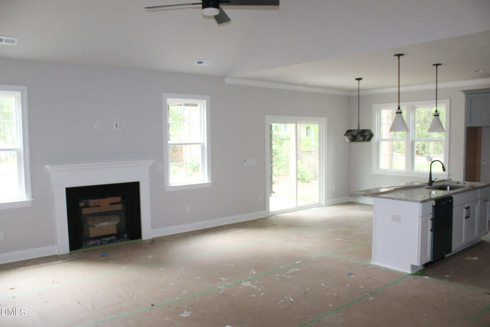Unfurnished open living space with a fireplace, large windows, sliding glass door, and kitchen island with hanging lights. Floor is covered for protection during renovation or construction.