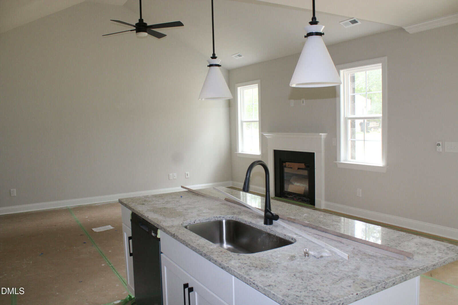 A modern kitchen with a granite island, white cabinets, black faucet, pendant lights, and an open living area with a fireplace, large windows, and unfinished flooring.