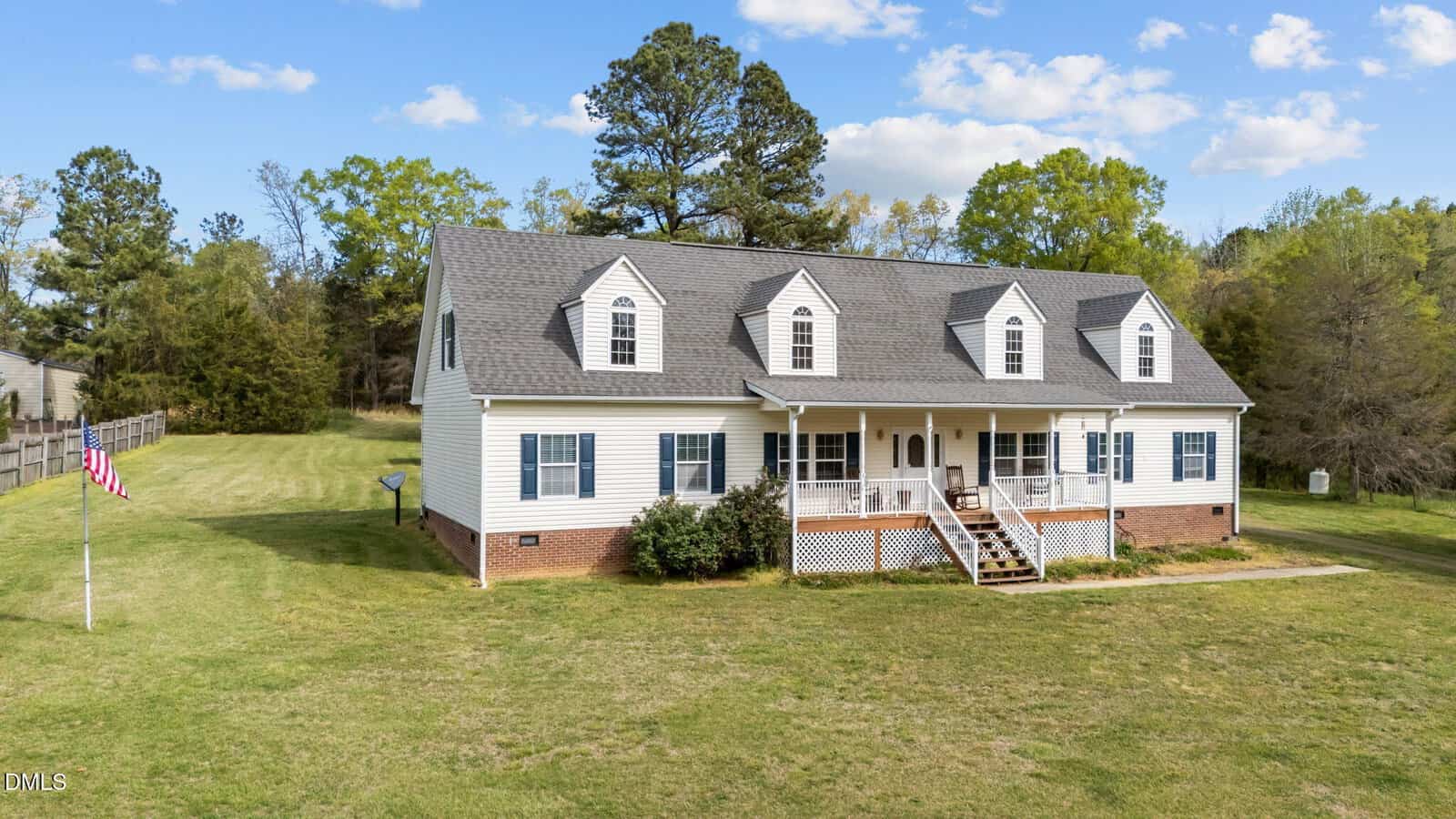 A large, white, two-story house with dormer windows and a covered front porch sits on a spacious grassy lawn with trees and a flagpole nearby at 1709 Enon Road, Oxford, under a blue sky with scattered clouds.