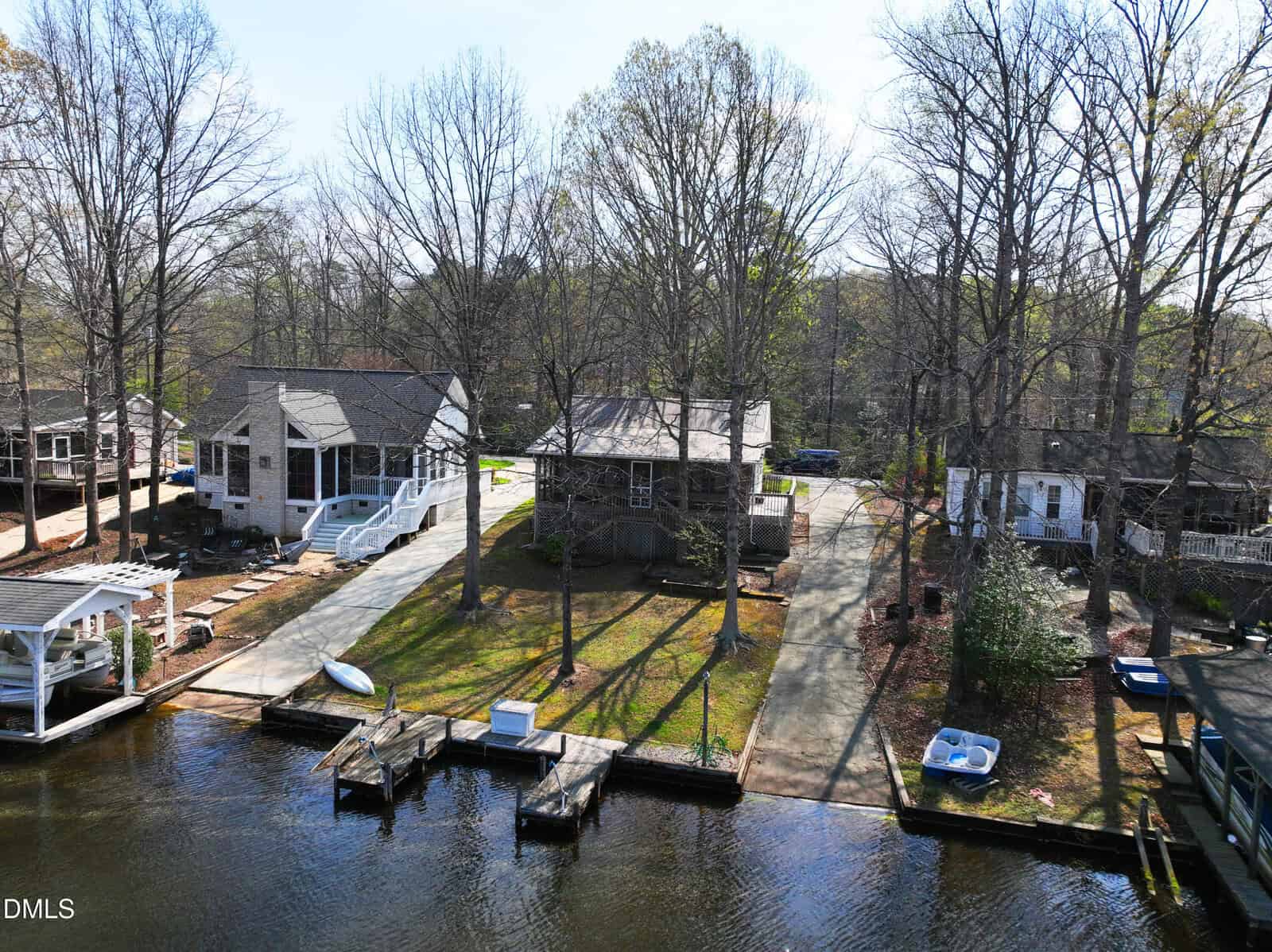 A waterfront neighborhood in Louisburg, featuring houses, docks, and boats along a calm lake. Trees without leaves line the shore near 150 Big Horn Cove, and driveways lead from the homes to the water. The scene suggests early spring.