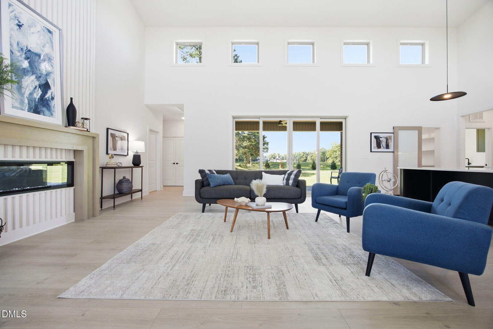 Modern living room with blue chairs, gray sofas, a round wooden coffee table on a large light rug, and a linear fireplace. Large windows let in natural light, and the decor is minimalist with neutral and blue tones.