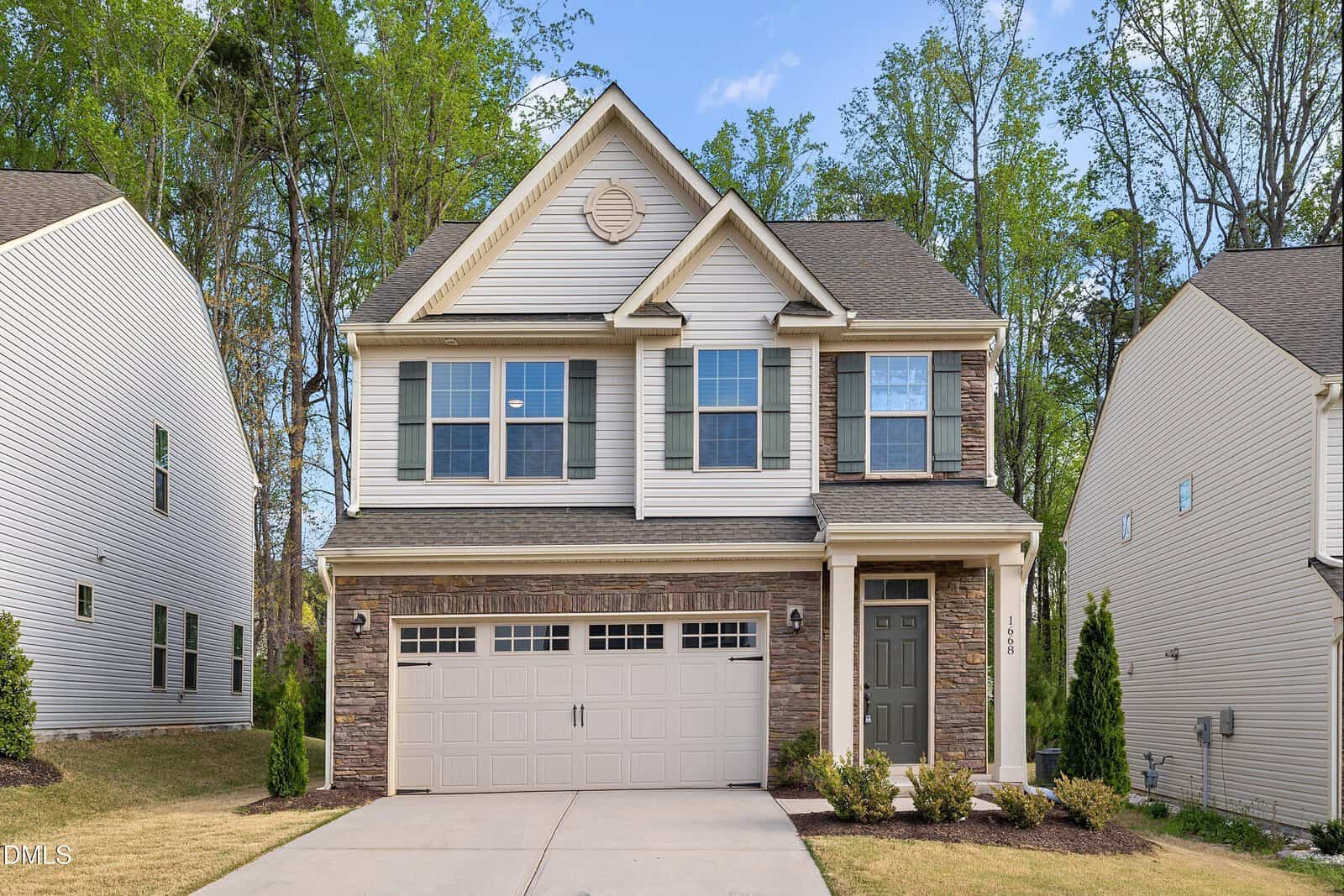 Two-story suburban house with a double garage, stone and siding exterior, neatly trimmed lawn, and trees in the background under a blue sky, located at 1668 Ripley Woods Street in the sought-after Wake Forest community.