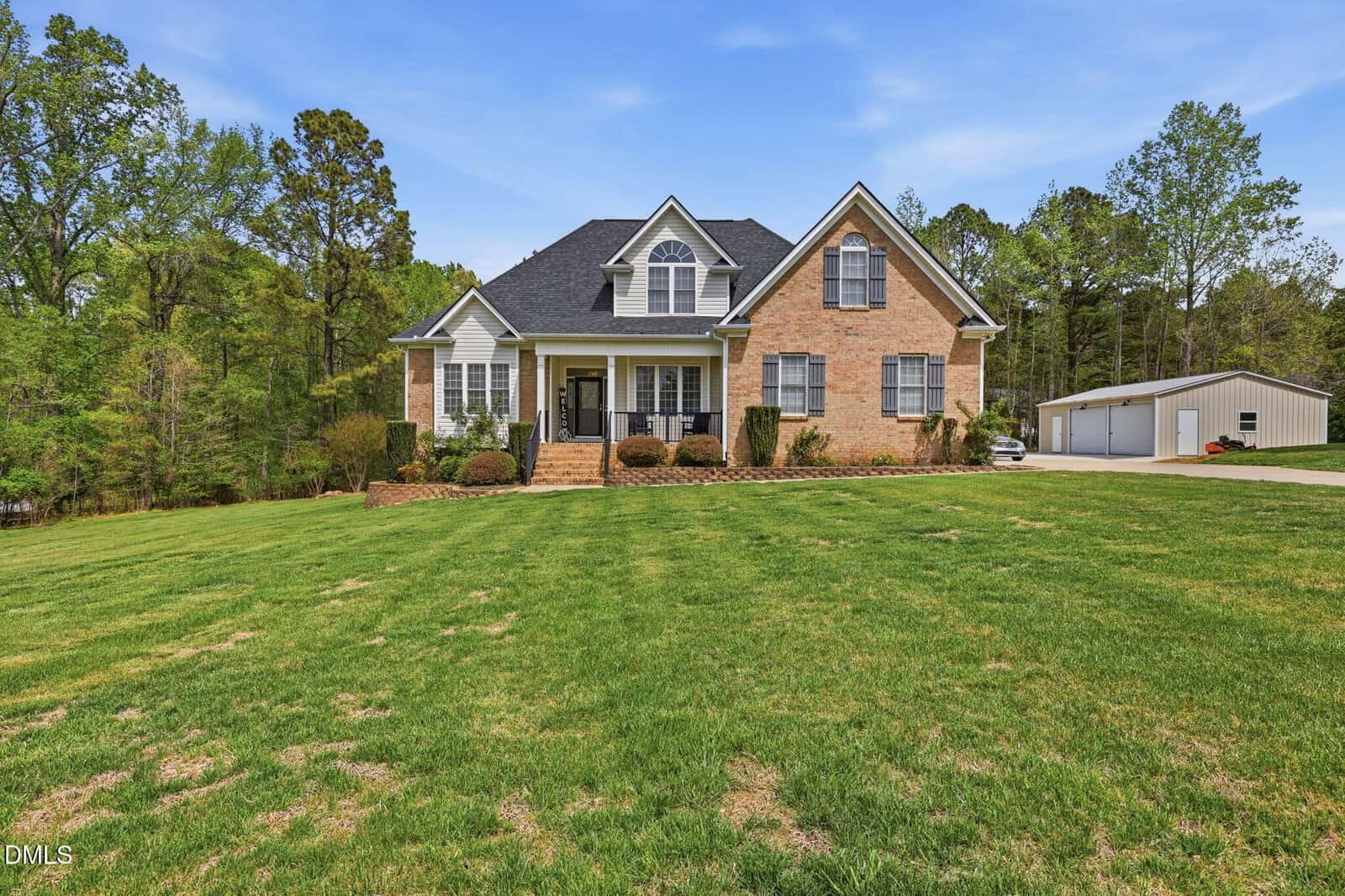 A large brick house with black roof, front porch, and manicured lawn, surrounded by trees at 3546 Saddle Ridge Road in Stem. A detached white garage is visible to the right under a clear blue sky.