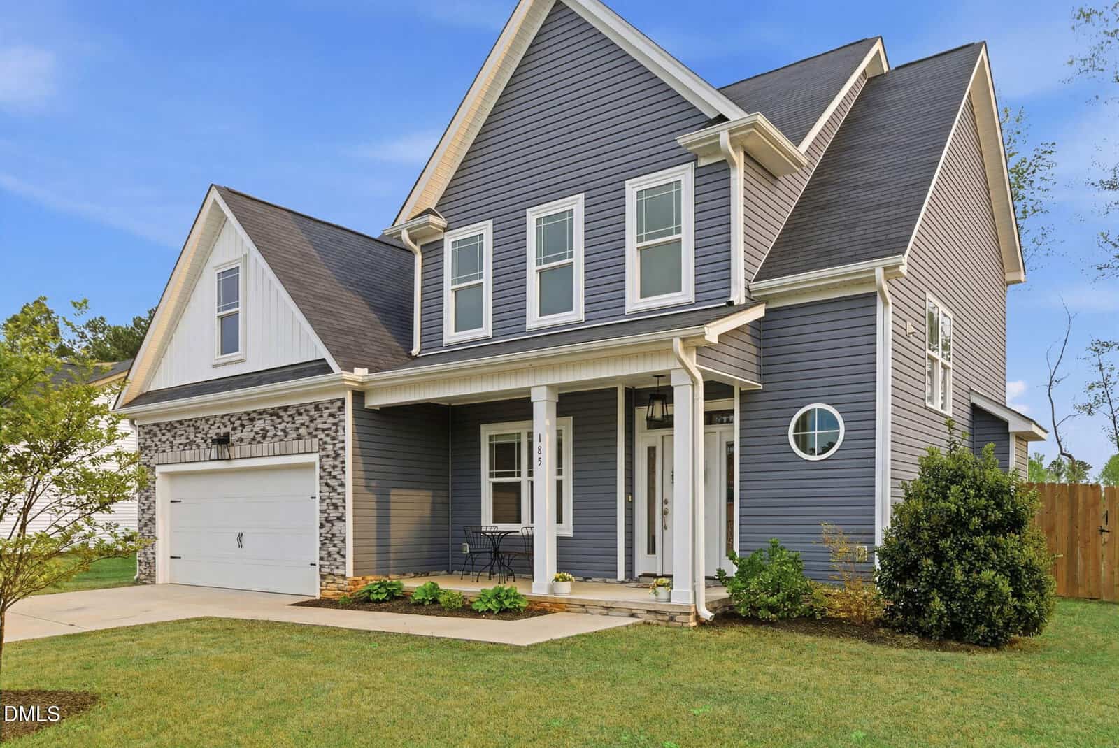 A two-story modern suburban house at 185 Stephens Way, Youngsville, with gray siding, white trim, a front porch, double garage, and gabled roof, set on a well-kept lawn with small shrubs and a wooden fence in the background.