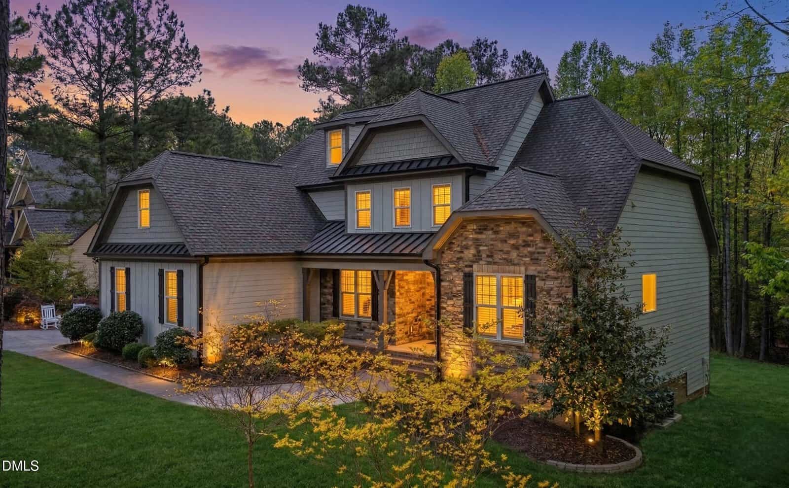 Two-story house with stone and siding exterior, large windows glowing with warm light, set among trees at sunset with landscaped front yard and walkway in the tranquil Creedmoor neighborhood at 3040 E East Bay Court.