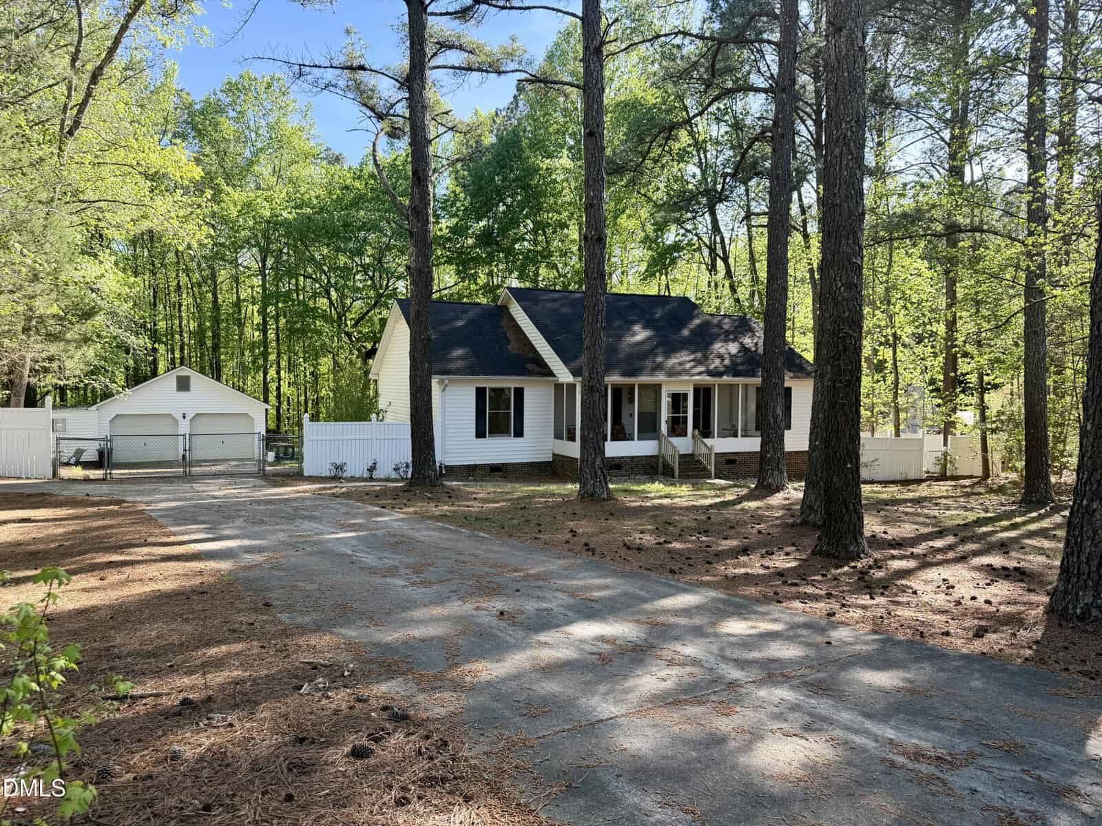 Nestled among tall trees in Franklinton, this white house with a dark roof sits gracefully at 4074 Old Franklinton Road. A white fence frames the property, complemented by a detached two-car garage. The driveway, surrounded by pine needles and shaded by trees, leads invitingly from the foreground to the charming home.
