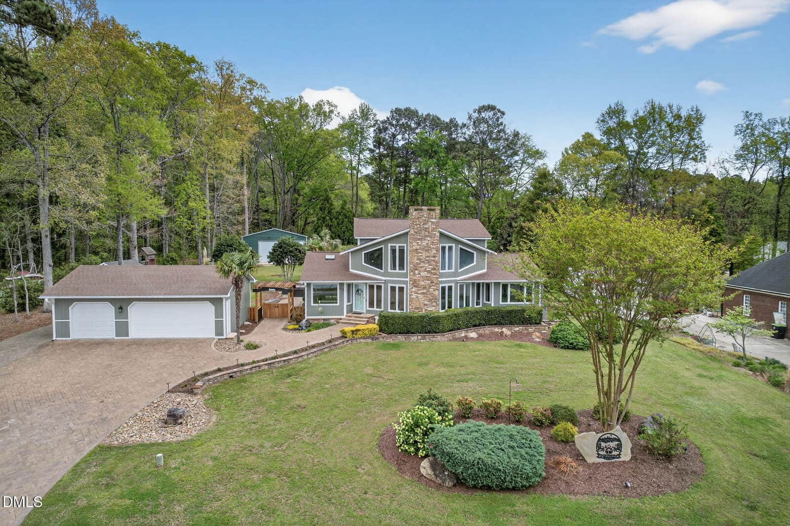 A contemporary house with large windows and a prominent stone chimney sits amid a well-kept lawn and landscaped garden beds at 30 Ray Avenue, Zebulon. A detached three-car garage is on the left, with trees forming the background.