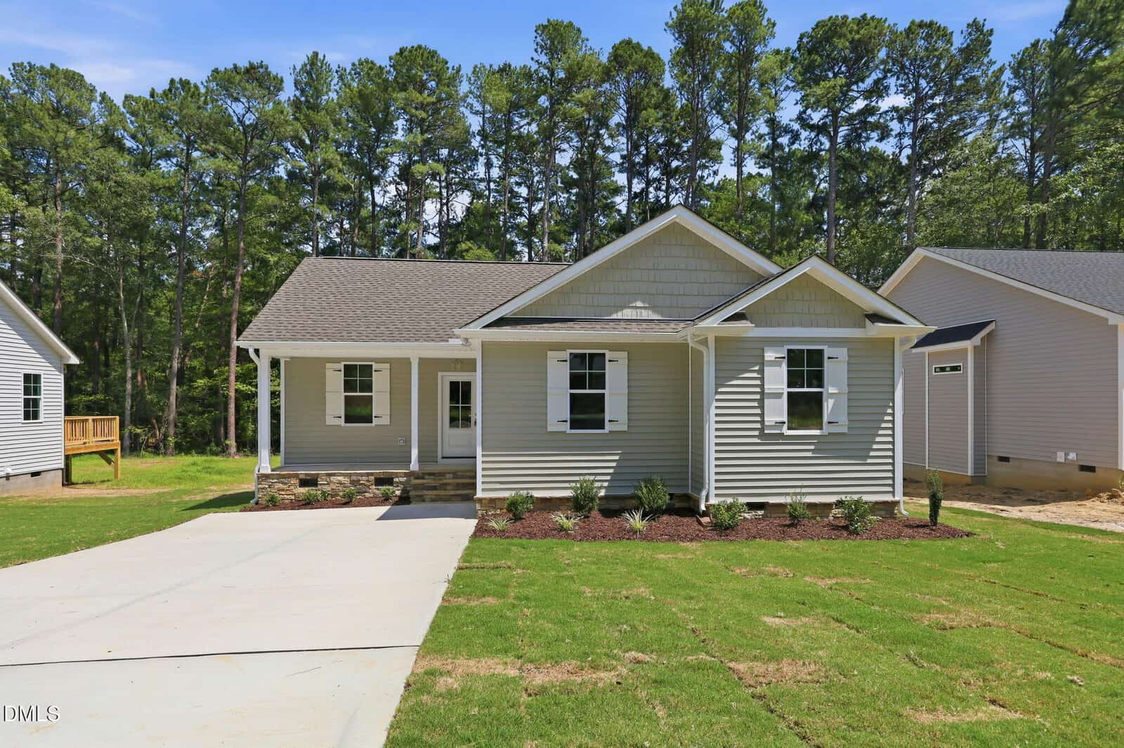 Single-story house with gray siding, white trim, and a covered front porch located in the heart of Oxford. This inviting home at 139 Seaman Street features a gable roof, attached garage, concrete driveway, and a green lawn bordered by mulch and small shrubs, with trees in the background.