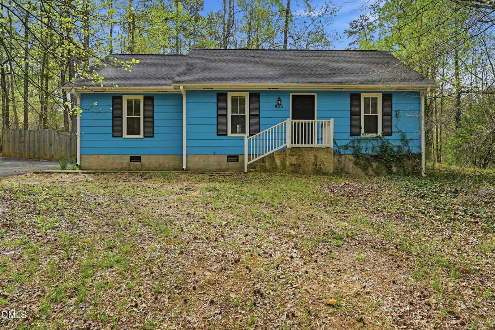 Charming one-story blue house with white trim, located at 943 Holden Road in Youngsville. Features a welcoming front porch with white railing, black shutters, and a gray shingle roof. Surrounded by trees and patchy grass, this home also includes a concrete foundation and a driveway partially visible on the left.